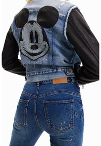 Jeansjacka med svarta ärmar, har slitna kanter och en stor grå Mickey Mouse-patch på ryggen; matchad med åtsittande blå jeans.