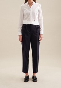 White cropped button-up shirt with long sleeves and a small embroidered detail, paired with dark navy high-waisted trousers and black loafers.