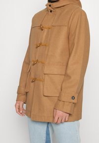 Brauner Wollmantel mit Kapuze, Knopfverschluss und zwei vorderen Taschen. Hat eine Länge bis zur Mitte des Oberschenkels und eine gewebte Textur.