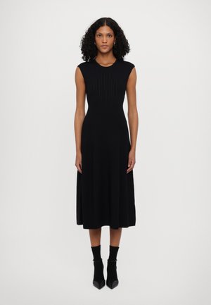 Robe noire midi avec un corsage côtelé et une jupe fluide lisse. Design sans manches, fabriquée en tissu doux. Portée avec des chaussettes chevilles et des talons pointus.