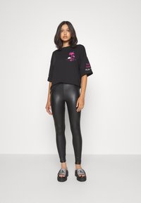 Sort oversized t-shirt med pink palmetto grafik, parret med skinnende sorte leggings og kraftige sorte sandaler med nitter.