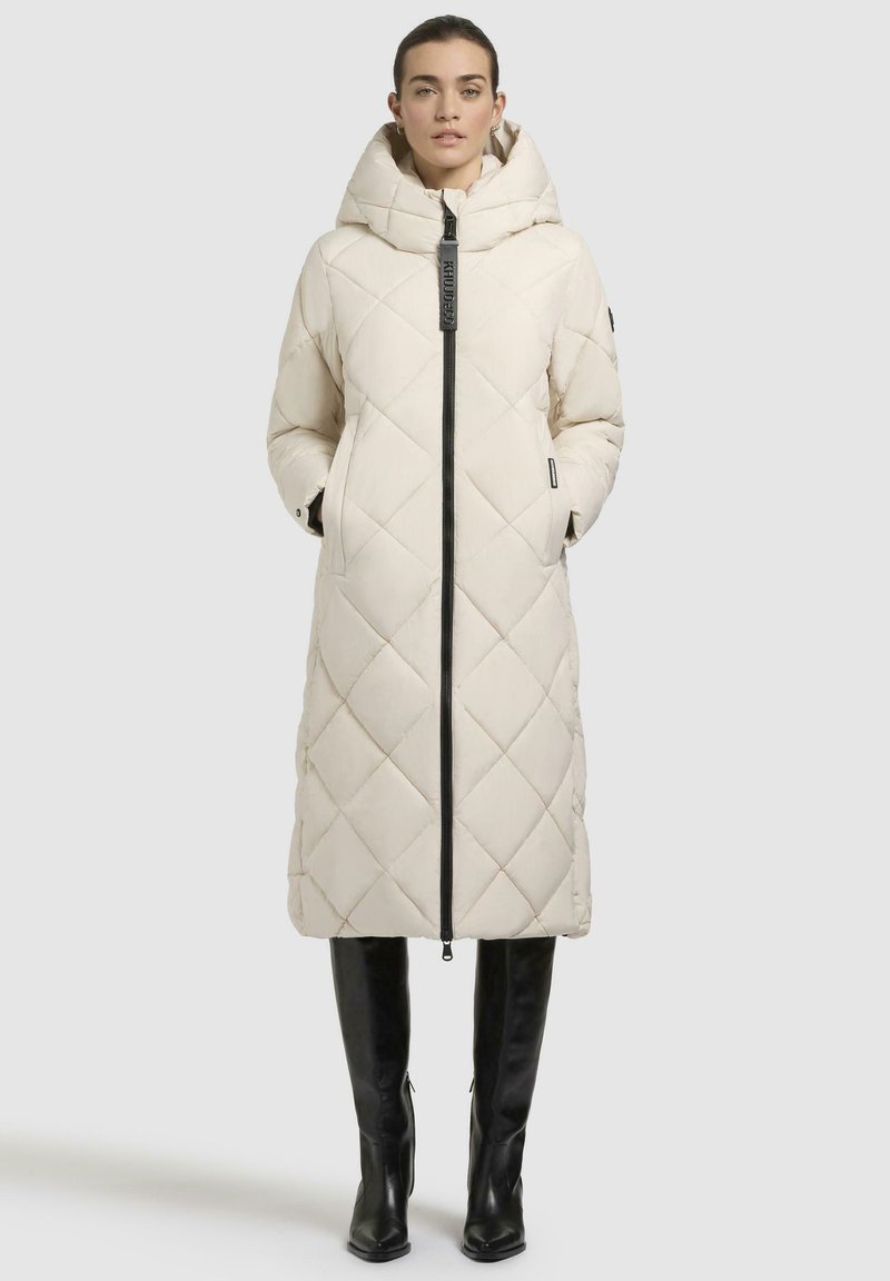 Lungo cappotto imbottito cremoso con cappuccio, zip frontale e tasche laterali. Presenta accenti neri e un motivo a diamante sul tessuto.