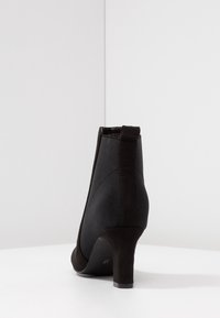 Bottine noire à cheville combinant tissu lisse et suède, avec un talon courbé et une languette arrière pour un enfilage facile.