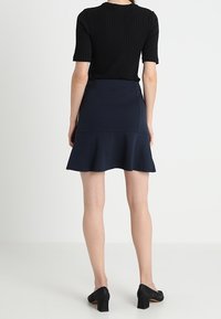 Haut noir à rayures, à manches courtes, associé à une jupe évasée bleu marine. La jupe présente une texture lisse et un discret détail à l'ourlet. Des chaussures noires à talons complètent le look.
