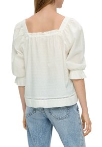 Blouse blanche à manches bouffantes avec des rayures texturées, un col froncé et des détails en ourlet festonné. Tissu doux et léger.