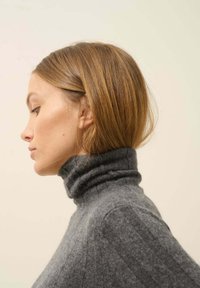 Szary sweter z golfem o prążkowanej fakturze, dopasowany krój, miękka tkanina i wysoki kołnierz widziany z boku na neutralnym tle.