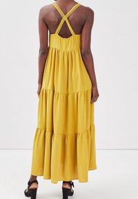 Robe maxi jaune à volants avec bretelles croisées, en matière douce ; silhouette fluide avec volants superposés à l'ourlet.