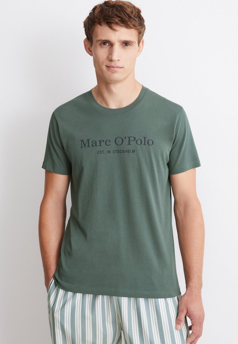 Vihreä puuvillapaidan t-paita, jossa on lyhyet hihat ja pyöreä pääntie. Etupuolella teksti "Marc O'Polo EST. IN STOCKHOLM" tummalla fontilla.