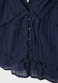 Tissu bleu foncé avec plis verticaux, bordure en dentelle, volants et une rangée de petits boutons ronds au centre.