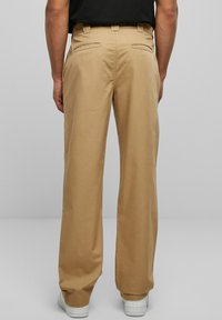 Khaki wide-leg trousers with a smooth fabric texture, featuring two back pockets and a zipper detail. Worn with white sneakers.