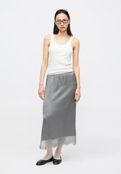 Fustă maxi din satin gri cu dantelă la tiv, asortată cu un top alb fără mâneci. Model purtând pantofi negri comozi; design minimalist.