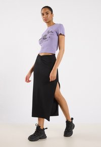 Purple ribbed crop top with black graphic design, paired with a floor-length black skirt featuring a side slit. Black chunky sneakers included.
