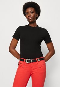 Svart, ribbestrikket topp med korte ermer kombinert med lyserøde jeans. Jeansene har frontlommer og et svart belte med en sølvspenne.