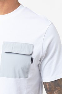 Bijela majica kratkih rukava sivoj džepom na prsima. Džep ima preklop i detalje šivanja. Tkanina izgleda glatko i lagano.