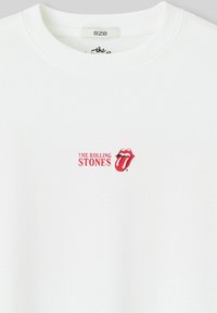 T-shirt en coton blanc avec un logo rouge "The Rolling Stones" et le dessin emblématique des lèvres au centre sur le devant. Col rond, style décontracté.