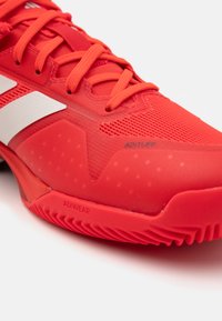 Red athletic shoe featuring a mesh upper with rubber accents, textured sole, and prominent branding, including "ADITUFF" and "ADIWEAR."