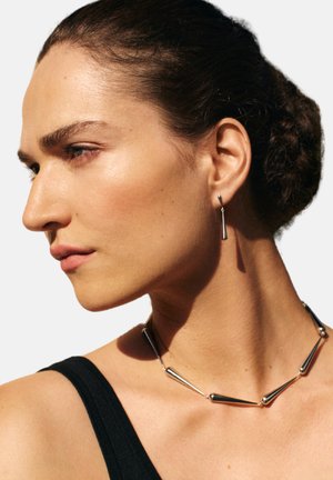 Silberfarbener Schmuck mit einem länglichen Kegel-Design. Die Halskette hat abwechselnde Segmente und wird von passenden Ohrringen in Tropfenform ergänzt.