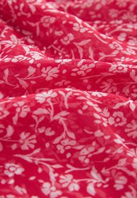 Tissu floral rouge avec des motifs de fleurs et de feuilles blanches. Léger, surface texturée, aspect légèrement froissé, adapté pour des vêtements ou de la décoration.