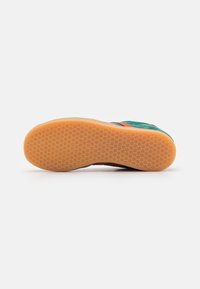 Sneaker with a green textile upper, orange and blue stripes, and a rubber outsole featuring a textured grip pattern.