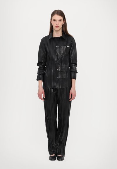 Fekete plissé ing és illő nadrág fényes, struktúrált anyagból, gombos eleje van, és a ing ujján egy zsebfedél található.
