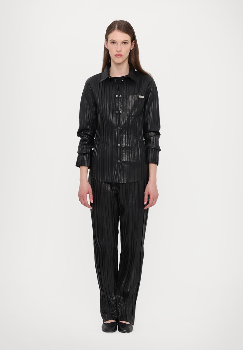 Svart plisserad skjorta och matchande byxor gjorda av ett glänsande, texturerat material, med knappframsidan och en bröstficka på skjortan.