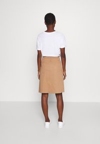 Brun bomuldsnederdel med lige snit og knælangt design, parret med en hvid T-shirt og hvide sneakers. Enkel og minimalistisk stil.