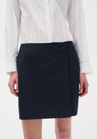 Granatowa spódnica o kroju kopertowym z pojedynczym zapięciem na guzik, wykonana z gładkiego bawełnianego materiału; charakteryzuje się delikatnym połyskiem i prostymi liniami.