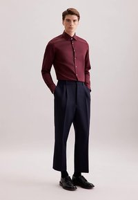 Camicia bordeaux abbottonata abbinata a pantaloni navy a vita alta. Scarpe eleganti nere lucide completano l'outfit. Tessuto liscio e vestibilità su misura.