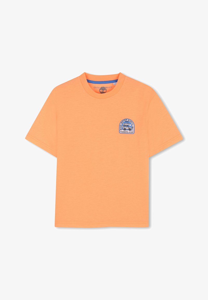 T-shirt orange à manches courtes avec un col rond et une petite écusson bleu représentant un véhicule et du texte sur le côté gauche de la poitrine.