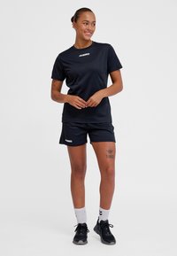 Czarny sportowy zestaw: koszulka i spodenki, wykonany z gładkiej tkaniny. Na koszulce i lewej nogawce znajduje się logo. Do kompletu czarne trampki i białe skarpetki.