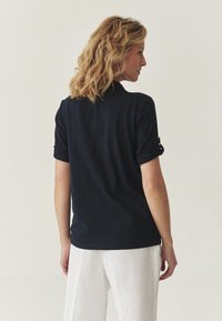 Polo cu mâneci rulate de culoare marină, realizat dintr-un material texturat. Design simplu cu guler și tiv drept.