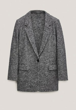Long blazer en tweed gris à revers crantés, fermeture à bouton unique noir et deux poches avant à rabat, posé à plat sur un fond neutre.