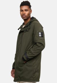 Green, long-sleeve jacket with a zip-up front, adjustable hood, and side pockets; features a black logo patch on the sleeve.