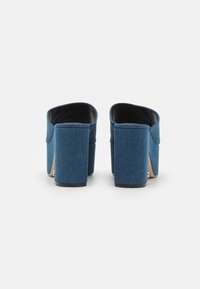 Mules con tacco alto in denim blu scuro, caratterizzati da una texture liscia, con un tacco largo e apertura posteriore. Design minimalista senza hardware visibile.