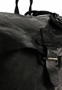 Bolso de cuero negro con superficie texturizada, que presenta una hebilla metálica plateada y detalle de correa. El diseño es simple y funcional.