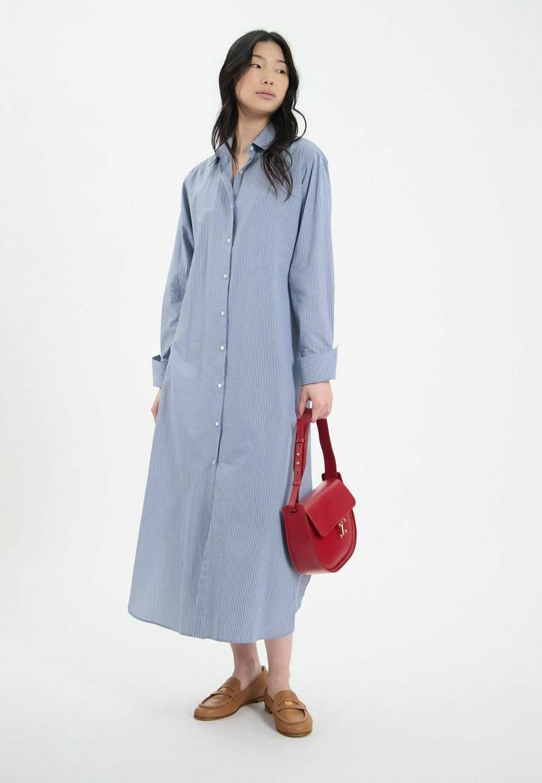 Robe chemise longue rayée bleu et blanc avec un devant à boutons, associée à des mocassins marron et un sac à main rouge. Tissu lisse et manches longues.
