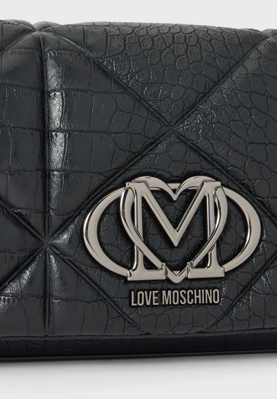 Близък план на черна дамска чанта Love Moschino с крокодилска текстура, сребристо преплетено лого и надпис на марката.