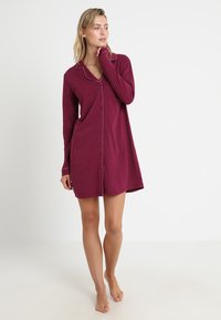 Maroon nightgown with long sleeves, button closure, and white piping along the collar. Soft fabric with a relaxed fit, knee-length design.