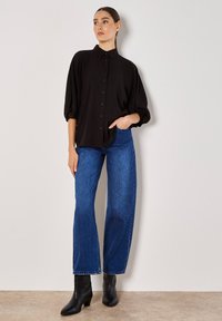 Schwarze Button-up-Bluse mit Puffärmeln, kombiniert mit blauen, hoch taillierten, weit geschnittenen Jeans und schwarzen Knöchelstiefeln. Einfaches, strukturiertes Design.