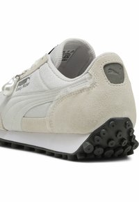 Sneaker Puma Easy Rider s bílým a béžovým semišem, texturovanými detaily a černou gumovou podrážkou s kruhovými hroty.