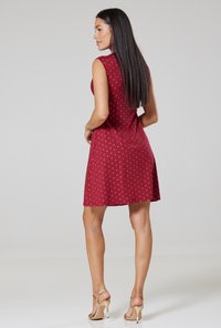 Burgundy sleeveless dress with white polka dots, slightly flared hem, and a smooth fabric. Worn with gold strappy heels.
