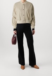 Beżowa bomberka z wełny z ribbowymi mankietami i dolnym wykończeniem, czarne spódnice o rozszerzających się nogawkach z ribbami, brązowe buty z ostrym noskiem oraz ciemnoczerwona torebka o fakturze.