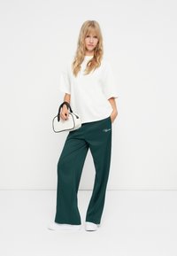 Tricou oversized alb, pantaloni largi verzi cu buzunare laterale și adidași albi. Geantă alb-negru cu mânere curbate.