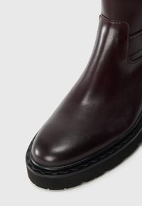 Botte de cheville en cuir bordeaux avec un bout arrondi, dotée d'une semelle en caoutchouc noir texturé et de subtiles accents de couture.