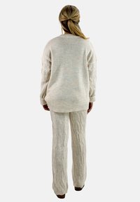 Strick-Zweiteiler in Creme, bestehend aus einem locker sitzenden Pullover und gemusterten Hosen mit Zopfstrickdesign, das vertikale Texturen präsentiert.