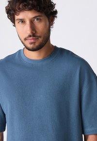 T-shirt in cotone blu a girocollo con maniche corte, caratterizzata da una finitura testurizzata e una vestibilità rilassata, mostrata su uno sfondo bianco semplice.