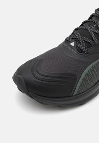 Zwarte sportieve schoen met een gestructureerde bovenkant, gestroomlijnd design, groene accenten en een stevige rubberen zool. Veters met versterkte oogjes.