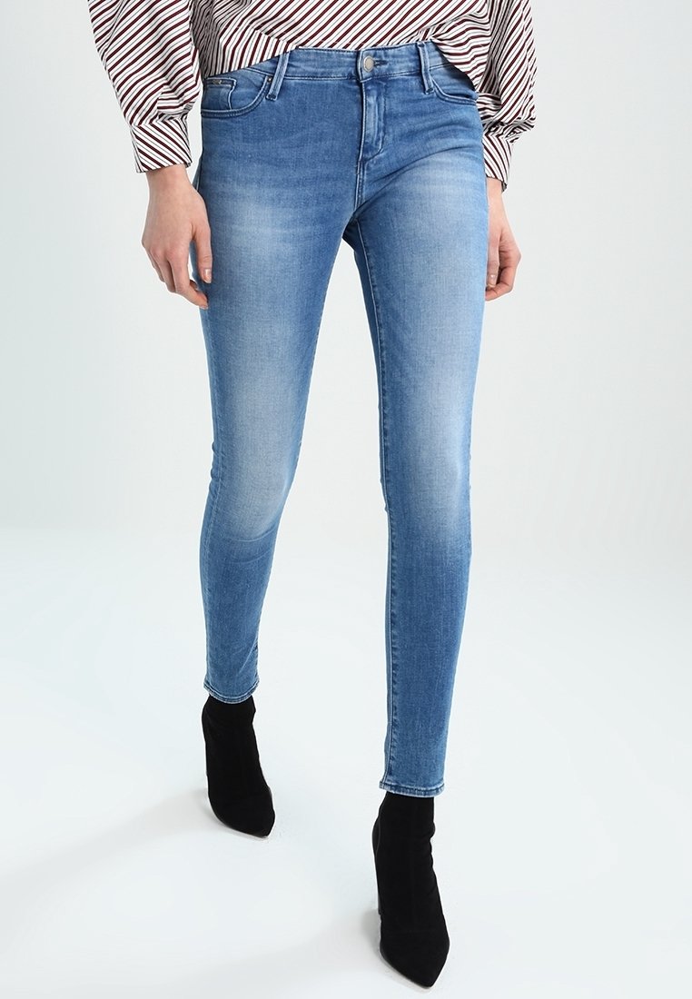 Kapeat siniset farkut, jotka on valmistettu denimi-kankaasta. Niissä on kulunut pesu, viiden taskun muotoilu ja etupuolen napitus. Yhdistetty mustien nilkkureiden kanssa.