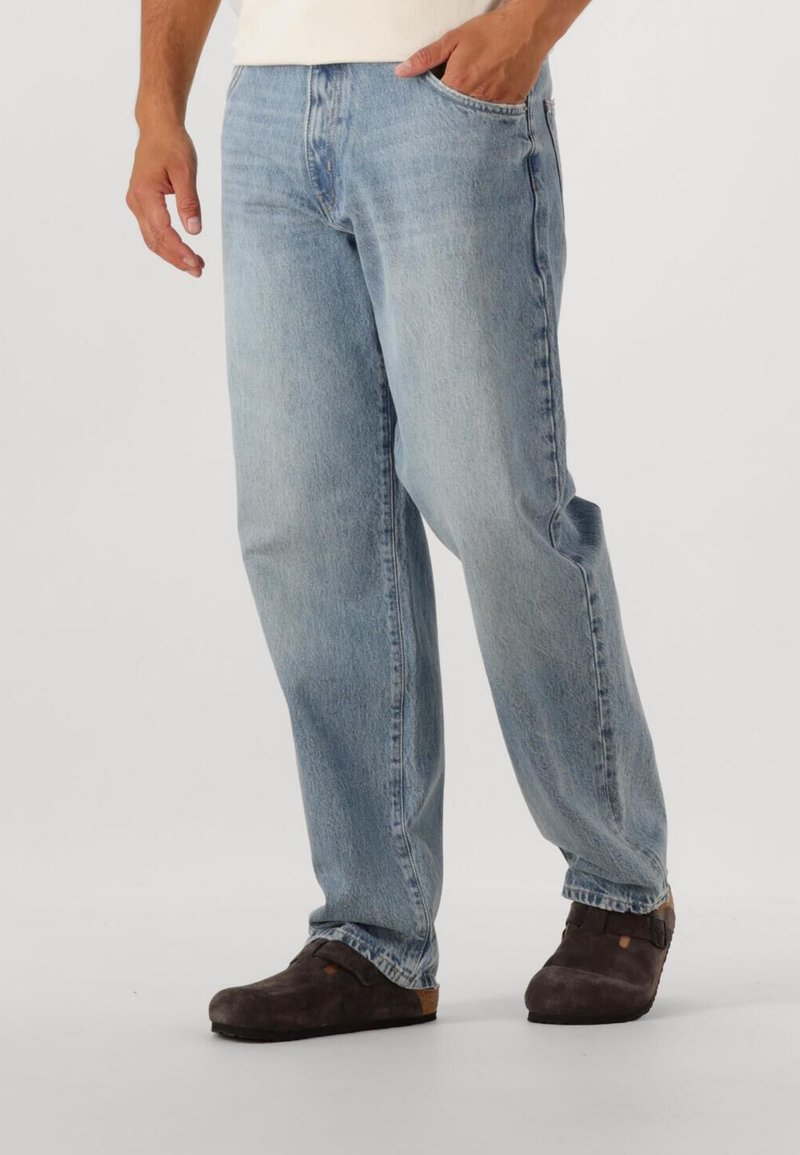 Ljusblå denimjeans med lös passform, femficksdesign och synlig sömnad, kombinerat med mörka träskor.