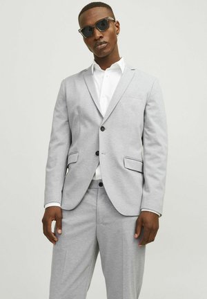 Light gray suit made of stretch fabric; features a notched lapel, two buttons, front pockets, and matching trousers, paired with a white shirt.